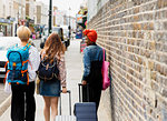 Young women friends with suitcases and backpack walking on urban sidewalk