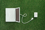 Electrical power socket on the grass and laptop with a plug, green renewable energy and power generation concept