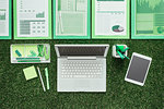 Laptop, tablet, office supplies and financial reports on the grass, green business and finance concept