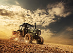 Farmer in the fields driving a tractor on fertile soil during a sunny summer day