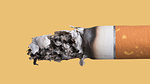 Cigarette burning close up on yellow background, stop smoking concept
