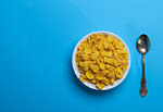 cornflakes in a white ceramic plate and an iron spoon on a blue background, top view, empty space