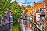 Bruges, Belgium. Medieval ancient houses made of old bricks at water channel with boats in old town. Summer sunset with sunshine and green trees. Picturesque landscape.