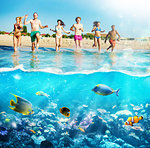 Group of friends run to the crystalline sea with colorful fishes. Concept of summertime