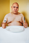 Photo of a large topless man waiting impatiently at a table for food.