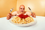 Photo of a large topless man about to eat his large plate of spaghetti.