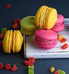 multicolored baked cakes of almond flour macarons on a white wooden board, black background, close up