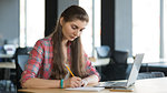 Portrait of a Serious Woman Writing in the Notebook while Working on Laptop in her Workplace.