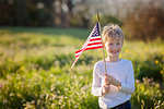 young boy holding american flag celebrating 4th of july, independence day, or memorial day in the park, copy space on left