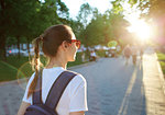 back view of a young attractive woman in white t-shirt with small city backpack at sunset on the walkway in park