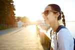 portrait of a young attractive woman in white t-shirt with small city backpack at sunset on the walkway on bay