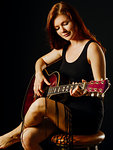 Photo of a young beautiful redhead woman sitting playing an acoustic guitar.