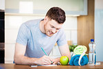 healthy lifestyle concept - man at home writing down training and sports nutrition plans