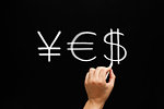 Hand writing YES with yen euro and dollar signs with white chalk on blackboard.