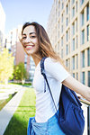 portrait of a young smiling attractive woman in white t-shirt with small city backpack at sunny day on city building background. woman poses in cityscape.