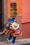 Man carrying straw bags and a stack of straw hats on his head to market in San Miguel de Allende, Mexico