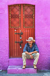 Mexican man sitting on stoop in front of purple building in Uriangato, Guanajuato, Mexico