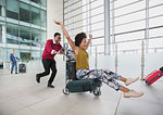 Playful couple running with luggage cart in airport