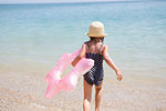 Girl carrying pink inflatable into sea, Scopello, Sicily, Italy