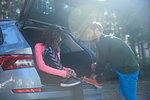 Male and female runners tying laces on car boot in sunlit forest