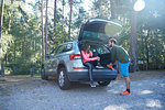 Male and female runners tying laces on car boot in sunlit forest