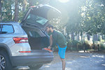 Male runner tying laces on car boot in sunlit forest