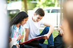 Female and male higher education students looking at  paperwork on college campus lawn