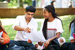 Female and male higher education students discussing  paperwork on college campus lawn