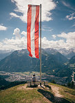 Boy sitting under Austrian flag contemplating mountain landscape, Bludenz, Vorarlberg, Austria