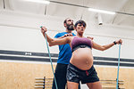 Trainer guiding pregnant woman using ropes in gym