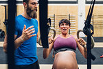 Trainer guiding pregnant woman using exercise equipment in gym