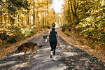Woman jogging with dogs in forest