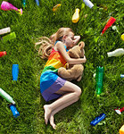 Young girl sleeping with her teddy bear in the plastic littered grass - pollution concept