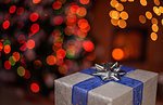 One christmas present with decorative ribbon in a dark room - with xmas tree and fireplace in background