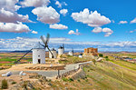 Wind mills and old castle in Consuegra, Toledo, Castilla La Mancha, Spain. Picturesque panorama landscape with road and view to ancient walls and windmills on blue sky with clouds.