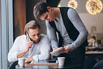 Portrait of two modern business people discussing work and using digital tablet during meeting in cafe on coffee break