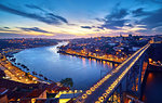 Porto, Portugal. Evening sunset panoramic view at nighttime town and Ponte de Dom Luis bridge with tramways. Coastline of river Douro with reflections of illumination in water and picturesque clouds on blue sky.