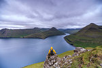 Hiker sitting on rocks looking at the fjords, Funningur, Eysturoy island, Faroe Islands, Denmark, Europe