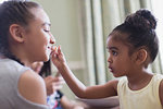 Cute toddler girl applying lip gloss to sister s lips