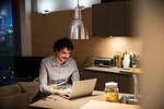 Man drinking white wine at laptop in apartment kitchen at night