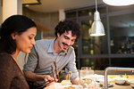 Smiling couple eating dinner with chopsticks in apartment kitchen