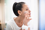 Woman applying moisturizer to face in bathroom mirror