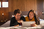 Happy young couple with headphones sharing digital tablet on bed