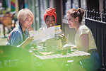 Young women friends looking at map, enjoying lunch at sunny sidewalk cafe