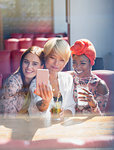 Young women friends drinking cocktails and posing for selfie in sunny restaurant