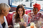 Young women friends using smart phone and drinking cocktails in restaurant