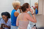 Young women roommates getting ready, applying makeup at bathroom mirror