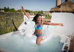 Playful, exuberant young woman in bikini sitting n inflatable pegasus in rooftop hot tub