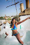 Portrait playful, carefree young woman in bikini on inflatable pegasus in sunny rooftop hot tub