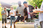 Male friends enjoying barbecue in sunny summer backyard